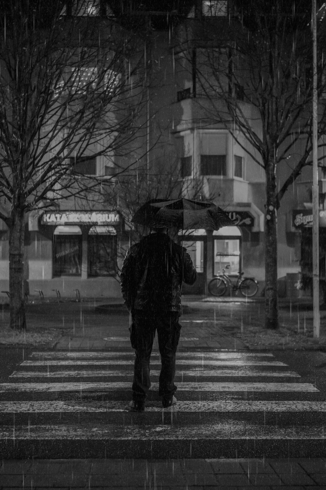 Silueta anónima de un hombre con gabardina y sombrero caminando bajo la lluvia nocturna